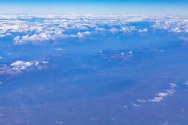 Bir uçak penceresinden görkemli dağların havadan görünüşü. Alplerin manzarası yukarıdan bir uçuşta görünüyor.