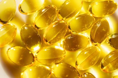 Sarı balık yağıyla dolu bir kase, Omega-3 yağ asitleri açısından zengin. Haplar oval şekillidir ve sarı renktedir. Beyaz bir yüzey üzerinde bir yığın halinde dizilmişler.