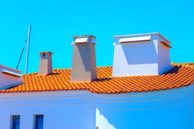 Döşeme çatılı ve bacalı beyaz bir bina. Canlı kırmızı çatılı geleneksel beyaz ev