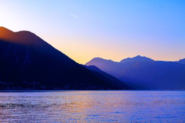 Karadağ sıradağları ve Kotor Körfezi alacakaranlıkta. Dağlar arka planda ve lagün ön planda.