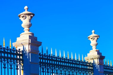 Dekoratif vazolar metal bir çitin üstünde. Vazolar uzun ve incedir ve çitin her iki tarafına yerleştirilmişlerdir.