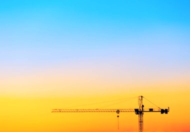 Turna, turuncu güzel bir gökyüzüne karşı gölgelenmiş. İnşaat alanındaki vinç makineleri