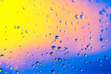 Üzerinde yağmur damlaları olan bir pencere. Yağmur damlaları pencerenin her tarafına saçılmış bulanık ve bulanık bir etki yaratıyor. Sahne sakin ve huzurlu, yağmur damlaları hafifçe düşüyor gibi.