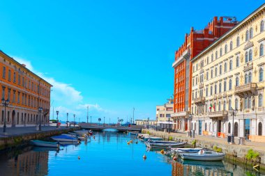 İtalya 'nın Trieste bölgesindeki yemyeşil ve tarihi binalarla çevrili manzaralı bir kanalda gezen tekneler. Bir sıra teknesi ve köprüsü olan su kanalı. 