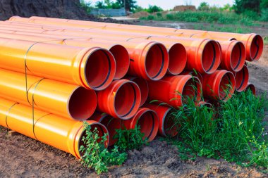 Turuncu borular üst üste istiflenmiş. Borular plastikle kaplı ve muhtemelen inşaat veya tesisat amaçlı kullanılacak. Organizasyon ve hazırlık kavramı