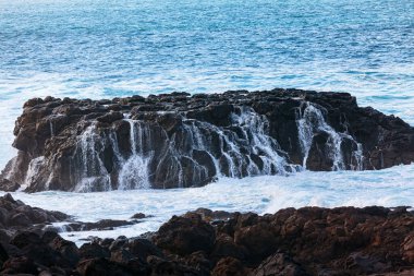 Okyanusta devasa bir kaya oluşumu. Deniz suyu dalgalı ve kayalar beyaz köpükle kaplı.