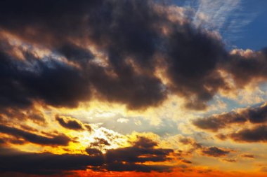Gökyüzü bulutlu ve güneş batıyor. Bulutlar karanlık ve gökyüzü mavi ve turuncu karışımı.