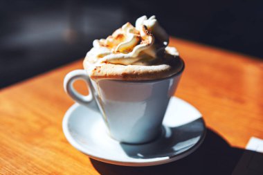 Krem şantili beyaz kahve fincanı ahşap bir masada duruyor. Krem şantili sıcak kahve.