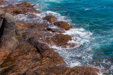 Okyanus sakin ve kayalar sudan dışarı fırlıyor. Dalgalar küçüktür ve su koyu mavi renktedir. Rocky sahili manzaralı doğal zemin