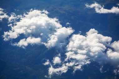 Bir uçak penceresinden görüldüğü gibi mavi gökyüzünde uzanan tüylü beyaz bulutların hava manzarası. Gökyüzü bulutlarla dolu, karamsar bir atmosfer yaratıyor. Bulutlar gökyüzüne dağıldı.