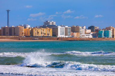 Arkasında deniz ve plaj olan Cadiz şehri, Endülüs İspanya. Okyanus dalgalı ve dalgalar çarpıyor. Kıyıdaki canlı şehir silueti Atlantik Okyanusu 'nun arka planında görünüyor.
