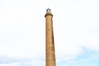 Deniz feneri bulutlu gökyüzüne karşı. Tepesinde ışık olan uzun kule.