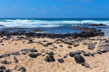 Tranquil beach scene showcasing rugged rocks along the shoreline. Beach is mostly empty, with only a few rocks scattered around. Scene is calm and peaceful, with the waves crashing in the background clipart