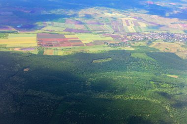  Uzakta bir köyü olan bir ormanın havadan görünüşü. Yeşil tarlaların ve ormanlık alanların muhteşem manzarası doğal bir manzara yaratıyor.