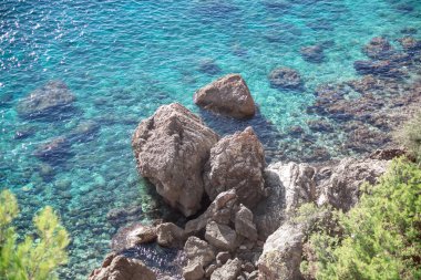 Rocky sahili doğal manzara ve sakin sularla çevrili. Arkasında açık mavi bir okyanus olan kıyı şeridi. Kayalar sahile saçılmış, resim gibi bir manzara yaratıyor.