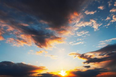 Yumuşak bulutlar ve güneş ışınlarıyla gün doğumu ya da batımı gökyüzü. Renkli bulutlarla huzurlu bir gün batımı. Gökyüzü mavi ve turuncunun bir karışımıdır. Sıcak ve huzurlu bir atmosfer yaratır.
