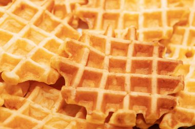 Parlak sarı desenli waffle tabağı. Sarı tabaklı bir yığın waffle. Waffle 'lar altın kahverengidir ve kıtır kıtır bir dokuya sahiptir.