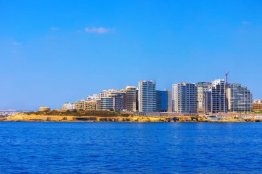 Malta 'daki Sliema şehri. Deniz kıyısında modern bir şehir. Deniz suyu, uzak şehirlerle çevrili gökyüzünü yansıtıyor.