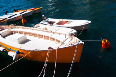 Sarı ve beyaz tekne halatla bağlanmış. Limandaki suda yüzen ahşap kayıklar.