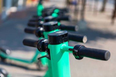 Kaldırımda düzgün park edilmiş, kullanıma hazır yeşil scooterlar. Gidona ve kontrol panellerine odaklan. Kentsel taşımacılık için paylaşılan elektrikli scooterların kullanılabilirliği ve konforu