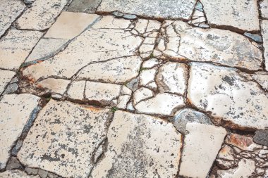 Kırık bir taş kaldırımın parçası. Taşlar düzensiz şekilli, çok sayıda çatlak ve çatlaklar var, bazı bölgeler daha aşınmış ve aşınmış görünüyor. Taş yüzeylerde zaman ve hava durumu etkileri