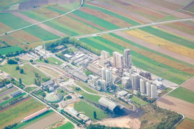 Avusturya 'daki çimento fabrikası yukarıdan görünüyor. Tarım alanlarıyla çevrili beton fabrikası. Tesis arasında birden fazla uzun silo, çeşitli binalar ve yollar ve demiryolu gibi altyapı yer alıyor.