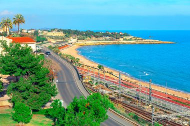 İspanya, Tarragona 'nın manzarası, kumlu bir sahil manzarası. Ön planda, kıyı şeridine paralel giden bir yol ve demiryolu hattı elektrikli bir demiryolu sistemiyle işliyor.