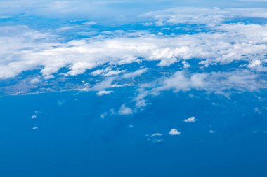 Ön planda geniş bir okyanus ve arka planda kısmen bulutlarla kaplı kara parçası ile kıyı bölgesinin havadan görünüşü. Kıyı şeridi bulutlardaki boşluklardan görülebilir.