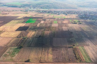 Her biri farklı ürün veya büyüme aşamalarını gösteren tarımsal tarlaların hava görüntüsü. Arka planda küçük bir yerleşim yeri var.