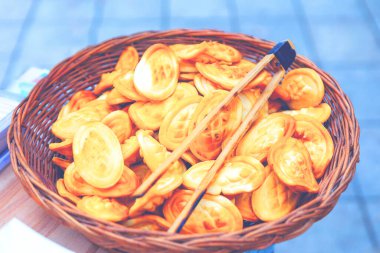 Oval şekilli hamur işleriyle dolu bir sepet. Tepede duran bir çift tahta maşa var. Hamur işlerinin servis edilmeye ya da satılmaya hazır olduğunu gösteriyor. Sepet kızarmış hamur parçalarıyla dolup taşıyor.