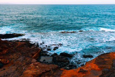 Rocky coastline with waves crashing against the shore. Water appears to be mix of blue and white due to foam created by waves. Rugged rocks and dynamic ocean waves makes beauty of coastal landscapes clipart