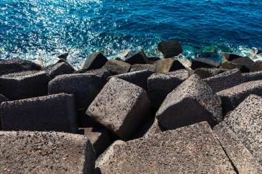 Sahil şeridi boyunca dizilmiş beton bloklar ve arka planda okyanus suyu görülüyor. Bloklar kıyı şeridini deniz kuvvetlerinden korumak için dalgakıran olarak kullanılır. Sahil mühendisliği erozyon kontrol yöntemleri.