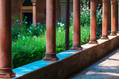 Güneşli manastır sütunları huzurlu bir bahçeyi çiçeklerle süslüyor, mimari zarafet ve doğal güzelliğin barışçıl bir karışımını sunuyor. Huzur, tarih veya kutsal mekan teması için ideal