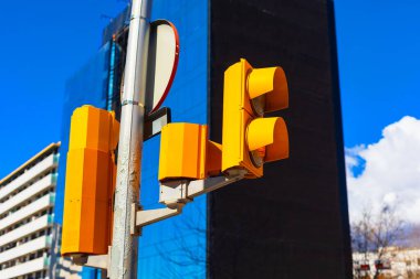 Mavi cam bina ve parlak gökyüzü karşısında sarı trafik ışıkları olan modern şehir caddesi manzarası. Şehir mimarisi, ulaşım altyapısı ve çağdaş şehir hayatı tasvir edilmiştir