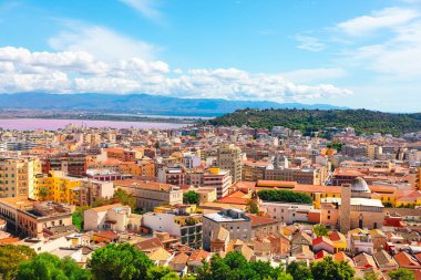 Güzel bir yaz gününde Cagliari, Sardinya İtalya 'nın panoramik manzarası. Tepelerle çevrili modern ve tarihi binaların ve arka planda bir su kütlesinin bulunduğu bir şehir manzarası.