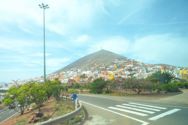  Pico de Galdar with a part of Galdar city in Gran Canaria, Canary Islands. Scenic view of a hilly town with colorful buildings spread across the hillside, road with a pedestrian crossing  clipart