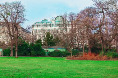 Viyana 'da, yapraksız ağaçlar ve çalılarla çevrili, cam kubbeli ve arka planda kemerli pencereleri olan büyük binalı bir park yeri. Doğanın bahar manzarası ve kentsel gelişim