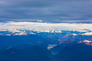 Maggiore Gölü 'nün nefes kesen manzarası. Karlı Alpler gün batımının ılık renklerinde parlıyordu. Su ve dağların çarpıcı zıtlığı, dingin güzelliği ve ihtişamı yakalıyor.