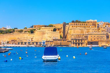 Malta 'nın Valletta kentinin manzarasında Akdeniz' in mavi sularına bakan tarihi kireçtaşı tahkimatları yer alıyor. Renkli şamandıralar arasında yüzen küçük tekne, kıyı manzarasına cazibe katıyor. 