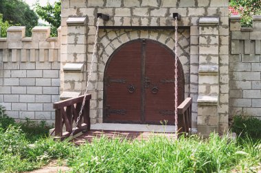 Ortaçağ tarzı ahşap asma köprüsü ve yemyeşil manzaralı çift kapılı bir kapı. Zincirler köprüyü askıya alıyor, kaleye görünüm, tarih ve masal temasını çağrıştırıyor