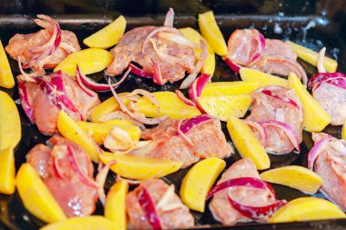 Çiğ et parçaları, patates parçaları ve kırmızı soğan dilimleriyle dolu pişirme tepsisi, hepsi baharatlı ve pişirilmeye hazır. Malzeme ve düzenlemelerin birleşimi kızarmış yemek için bir hazırlık öneriyor