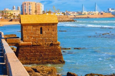 İspanya 'nın Cadiz kentinde engebeli kıyı şeridi ile harmanlanmış tarihi kale okyanusun kıyısında duruyor. Arka planda, modern binalar, kumlu plaj ve çarpıcı kablo destekli köprü kontrastı