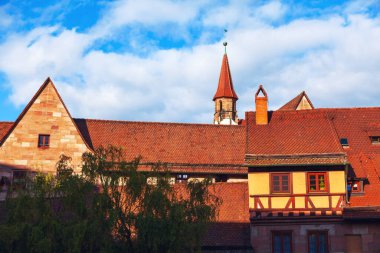 Büyüleyici Nuremberg eski kasabası kiremitli çatıları ve tarihi bir duyguyu çağrıştıran taş ve kereste çerçeveli binaları var. Bulutlu gökyüzü, manzaranın zamansız çekiciliğini artıran pitoresk bir arkaplan görevi görüyor