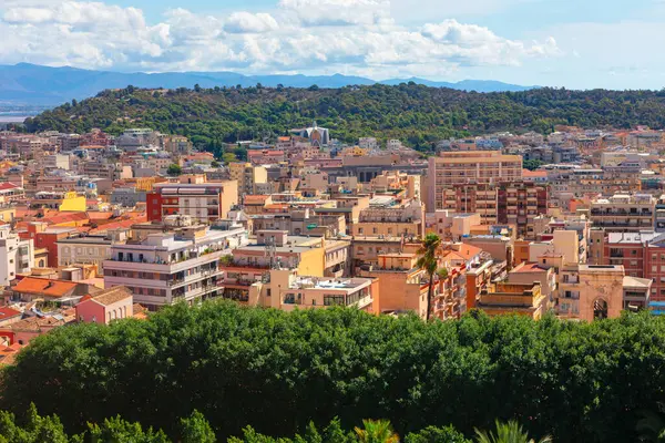 İtalya 'nın Cagliari kentinin panoramik manzarası, verimli yeşilliklerle çevrili modern ve geleneksel binaların uyumlu bir karışımı. Manzaralı tepe manzarası derinlik katıyor ve şehir manzaralı sahil cazibesini vurguluyor.