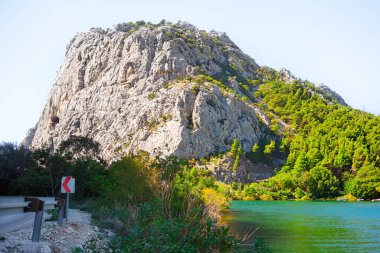Cetina Nehri ve Hırvatistan 'daki Omis Dağı. Görkemli kayalık dağ yeşilliklerle bezenmiş, yukarıdaki berrak göle karşı kurulmuş, ahenkli ve sakin doğal bir manzara yaratıyor.