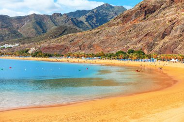 Santa Cruz, Tenerife, Kanarya Adaları 'ndan Playa de Las Teresitas. Kumsal berrak sular boyunca kıvrılır, insanlarla ve şemsiyelerle dolup taşar. Çarpıcı sahil manzarası, seyahat fotoğrafçılığı için mükemmel.