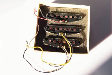 Kırmızı çubuk parçalı üç siyah tek bobinli gitar parçası köpük kaplı bir kutuda oturur ve yüzeyde gölgeler bırakır. Her pikaptan kablolar uzanıyor, elektro gitara bağlanmaya hazır.