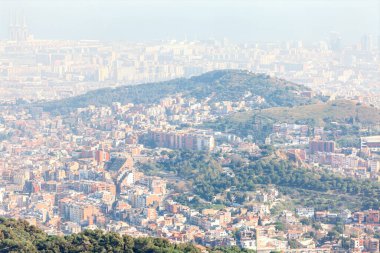 Barselona 'nın panoramik görüntüsü şehir yoğunluğunu sisli bir gökyüzünün altındaki yeşil tepe ile harmanlıyor. Şehir Balearic kıyısına doğru genişliyor, doğa ve modern mimarinin canlı karışımını gözler önüne seriyor.