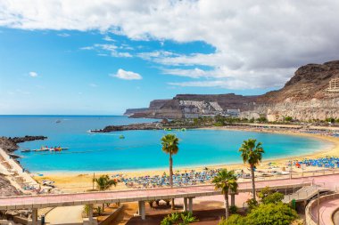 Gran Canaria 'da Playa de Amadores, altın kum ve turkuaz sularla dolu bir plaj engebeli kayalıklar ve renkli şemsiyeli palmiye ağaçları. Köprü ile manzara yürüyüşü plajı tatil köyüne bağlıyor 
