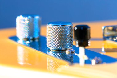 Gitar kontrol düğmeleri, metalik hacimli ve renkli bir yankesiciye monte edilmiş yüzeyi olan ton düğmeleri. Hafif gitar gövdesindeki parlak metal topuzlar. Çükler elektro gitarı işaret ediyor.
